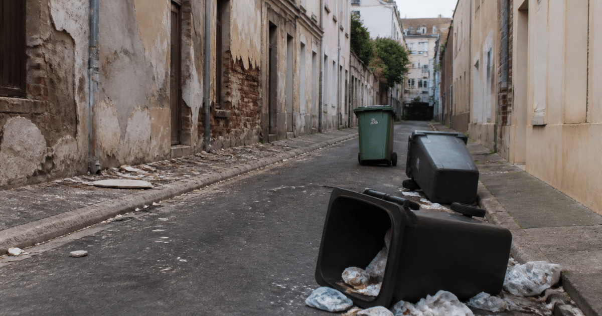 Rue urbaine degradee avec facades deteriorees et poubelles renversees