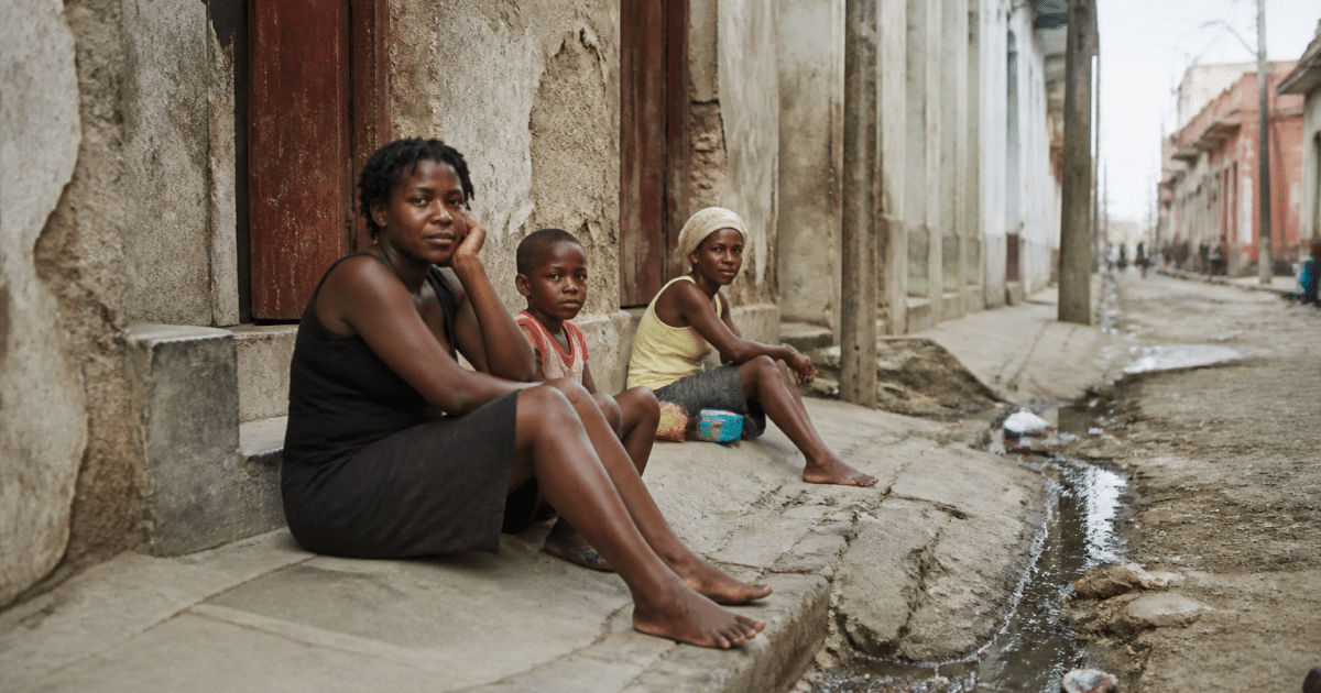 rue sombre avec batiments delabres et habitants assis au sol