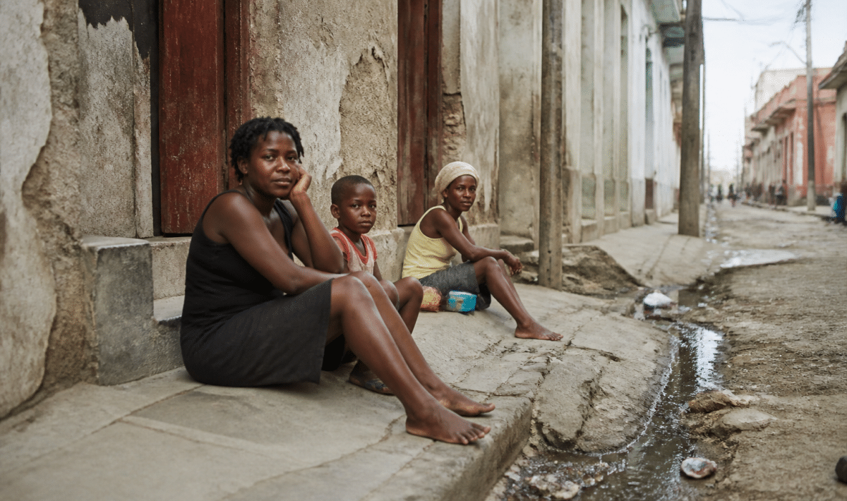 rue sombre avec batiments delabres et habitants assis au sol
